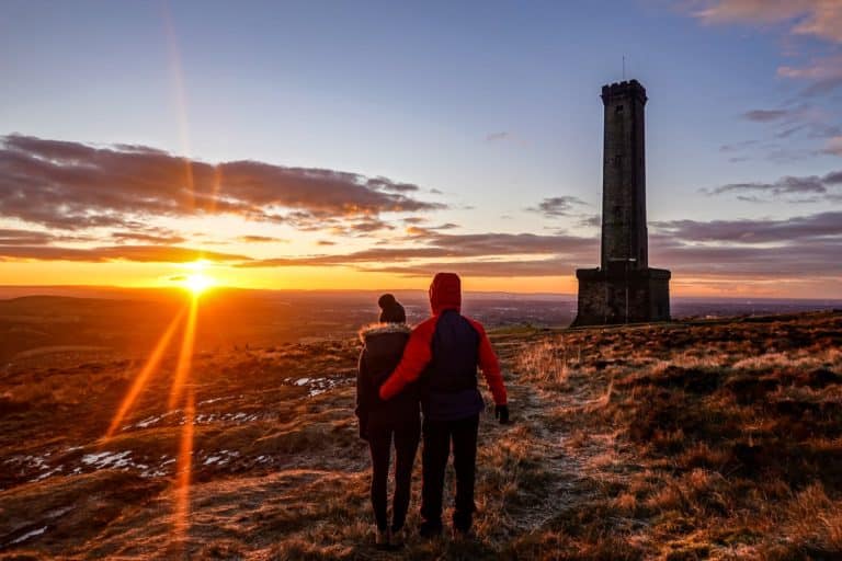 Beck and Dan watch sunrise during a walk, standing by Peel Tower on Holcombe Hill