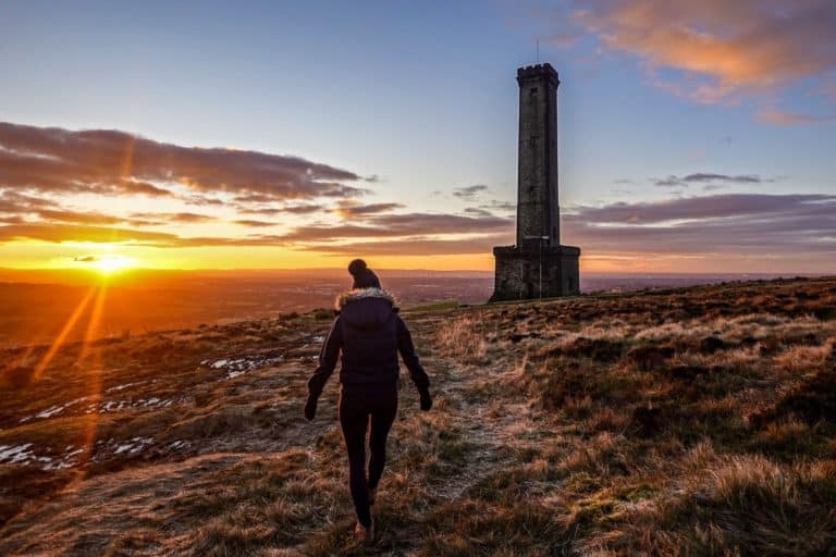 Beck walks towards Peel Tower on Holcombe Hill during sunrise