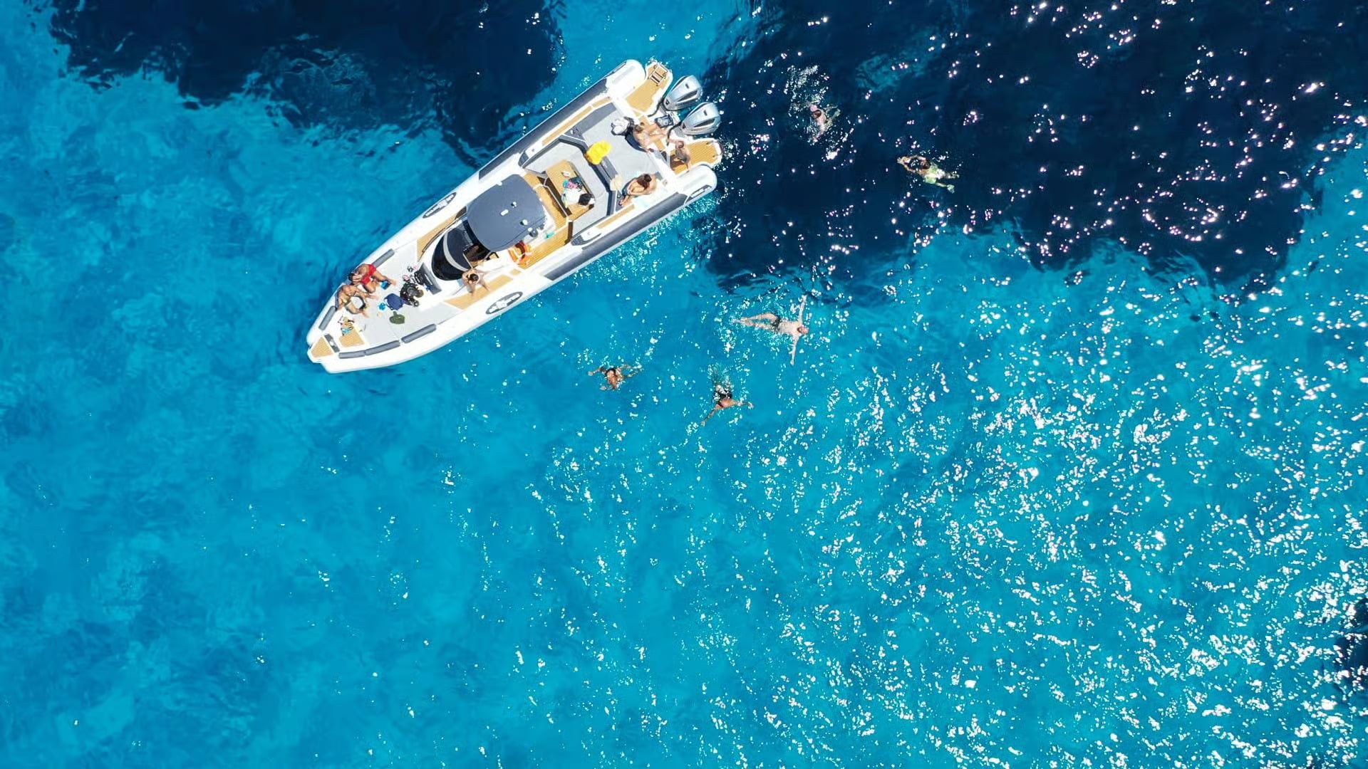 An aerial shot of a boat and people swimming in clear water