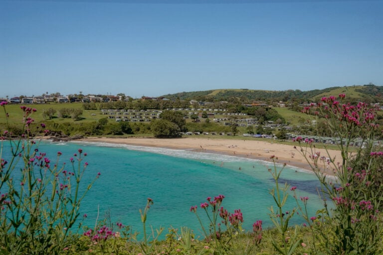 A beach in Kiama with turquoise-coloured water backed by a holiday park with caravan and camping sites