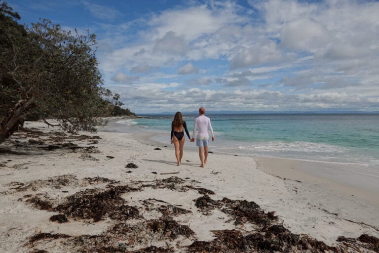 Man and woman walk along Murrays Beach in Booderee National Park