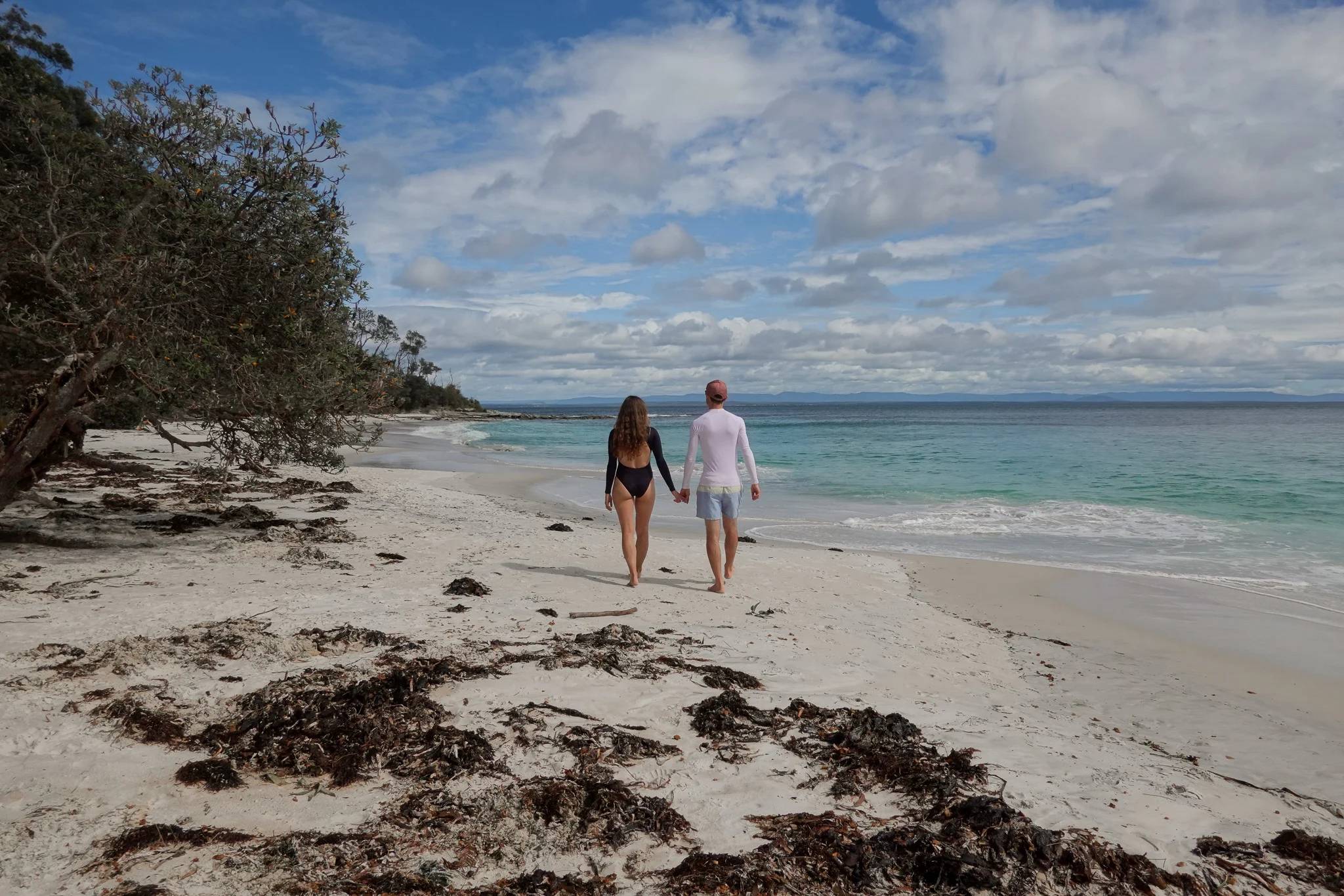 Man and woman walk along Murrays Beach in Booderee National Park