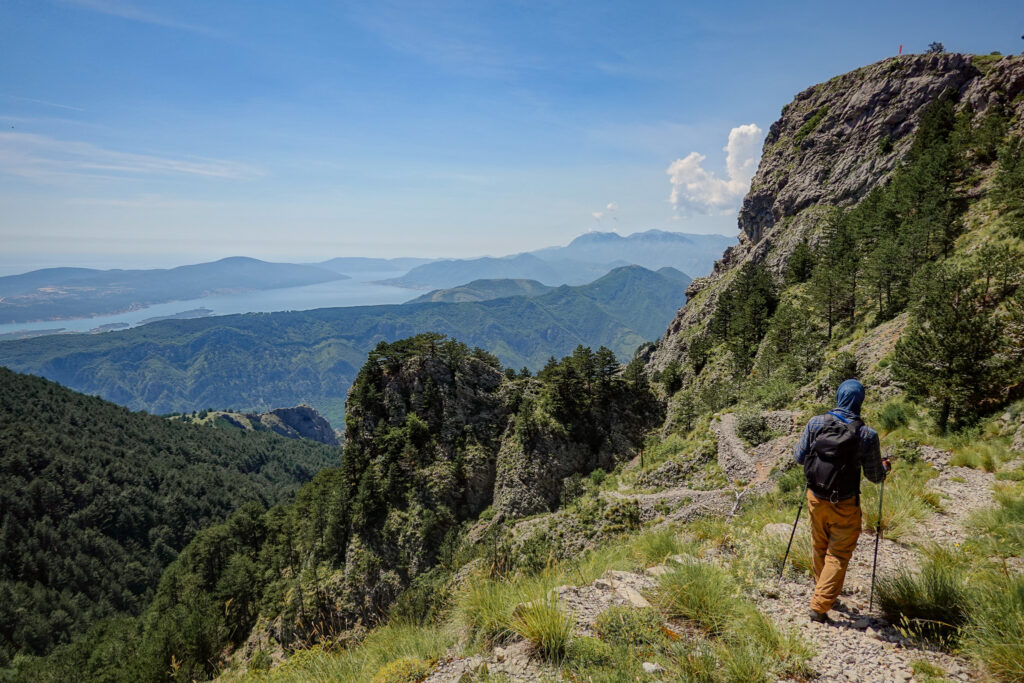 Hiker descends Pestingrad Peak surrounded by green forest and the sea beyond
