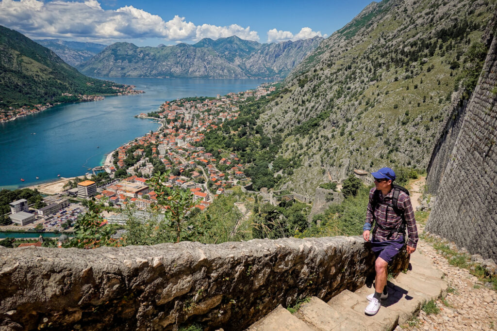 Man hikes up the stone steps on the Kotor Fortress walk with views of Kotor Bay and the old town below