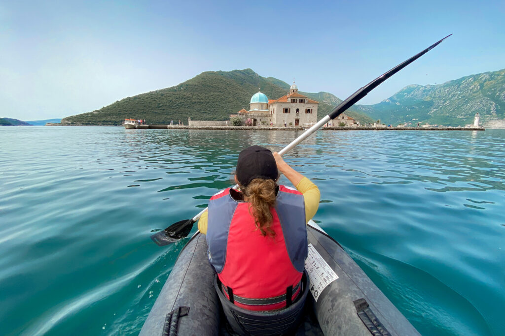 Woman kayaks towards Our Lady of the Rocks in Montenegro