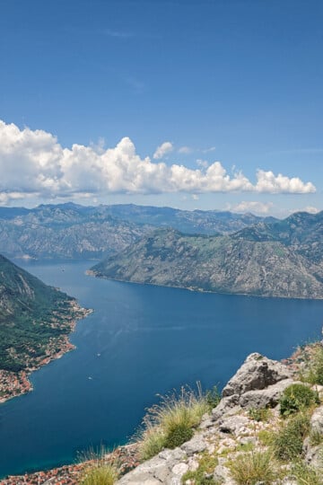Hiker stands on the mountain edge high above the blue waters of Kotor Bay, surrounded by mountain peaks of Montenegro.