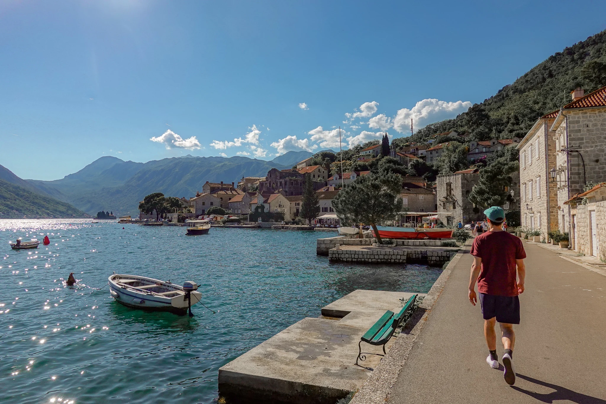 Man walks along Perast waterfront street in sunny weather