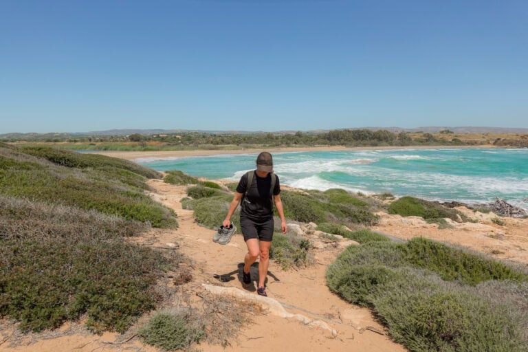 Beck holds her shoes as she walks by the coast in an area called the Vendicari Nature Reserve