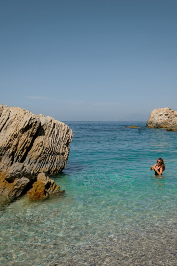 Beck stands and walks with the water of Kroreza Beach up past her waist