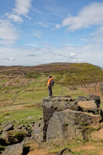 Beck stands on one of the sandstone crags overlooking a hill during a walk called the Wainstones Walk