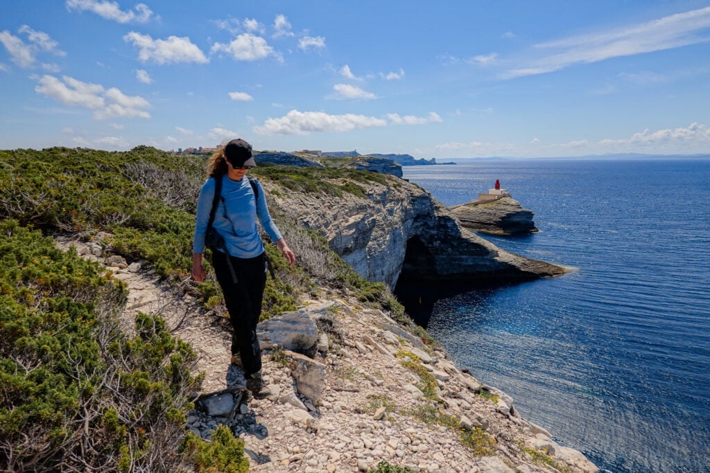 Beck walks on a coastal trail, heading away from red and white coloured lighthouse called the Madonetta Lighthouse
