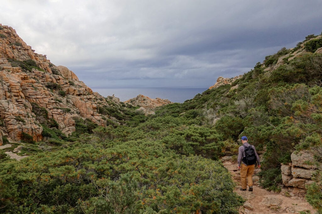 Dan walks towards dark grey clouds upon the horizon on a trail called Sentier de Fenu on a cape called Capo di Fenu in Bonifacio