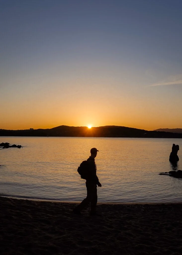 Dan walks along a beach during sunrise on a beach on Sentier Littoral des Bruzzi in Corsica