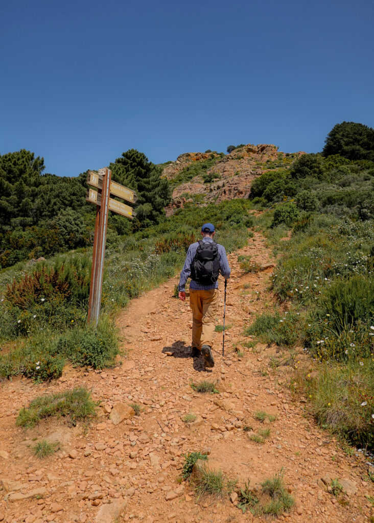 Dan hikes past a waymarking sign on a rocky trail ascent during the Calanques de Piana Hike