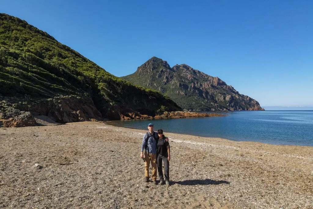 Dan and Beck embrace on a beach during a walk in Corsica called Sentier du Facteur Girolata
