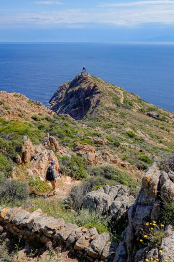 Dan walks down a trail approaching a lighthouse on Pointe de la Revellata