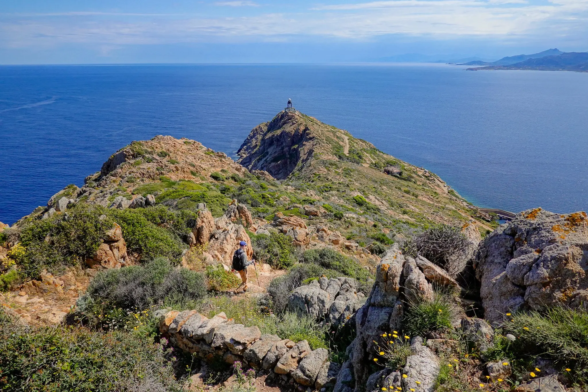 Dan walks down a trail approaching a lighthouse on Pointe de la Revellata