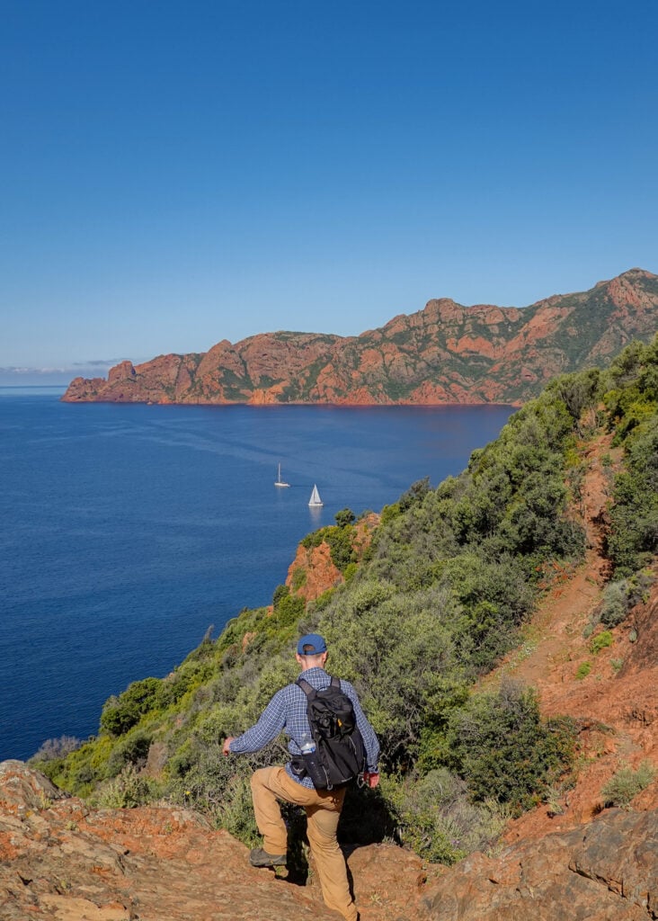 Dan is stepping down on a rocky coastal trail in Corsica called Sentier du Facteur Girolata