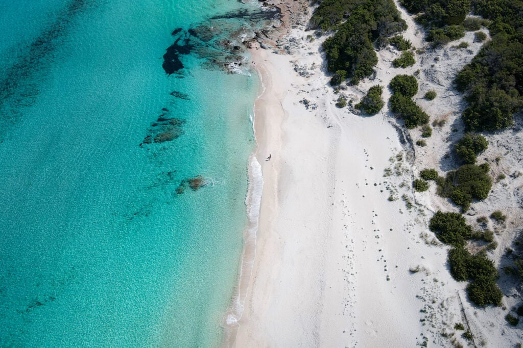 An aerial shot of Beck and Dan walking on a white sand beach during a walk called Sentier des Douaniers Saint-Florent in Corsica