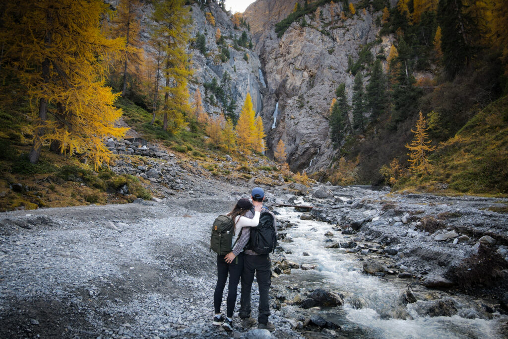 Beck and Dan embrace, while looking at a waterfall called Sertig Waterfall