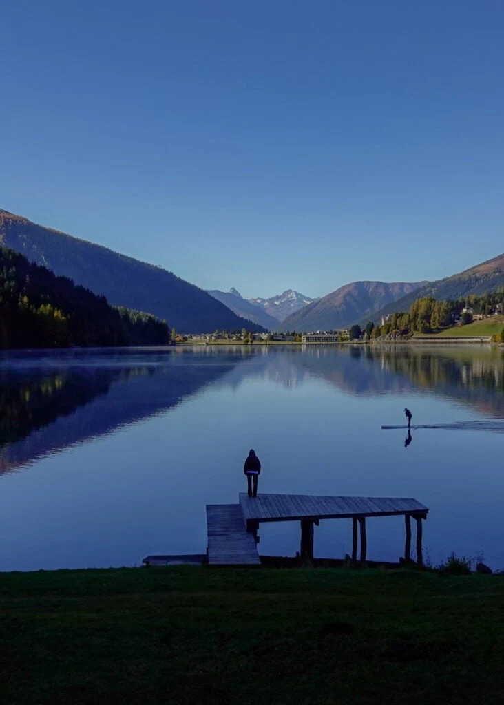 Beck stands on a wooden jetty near the lake during a walk called Davosersee Rundweg (AKA Lake Davos Trail)