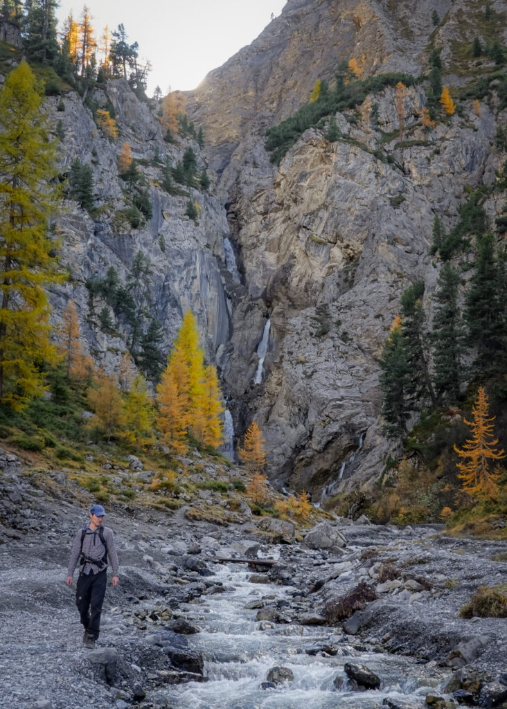 Dan walks by a stream fed by a waterfall in the distance called Sertig Waterfall