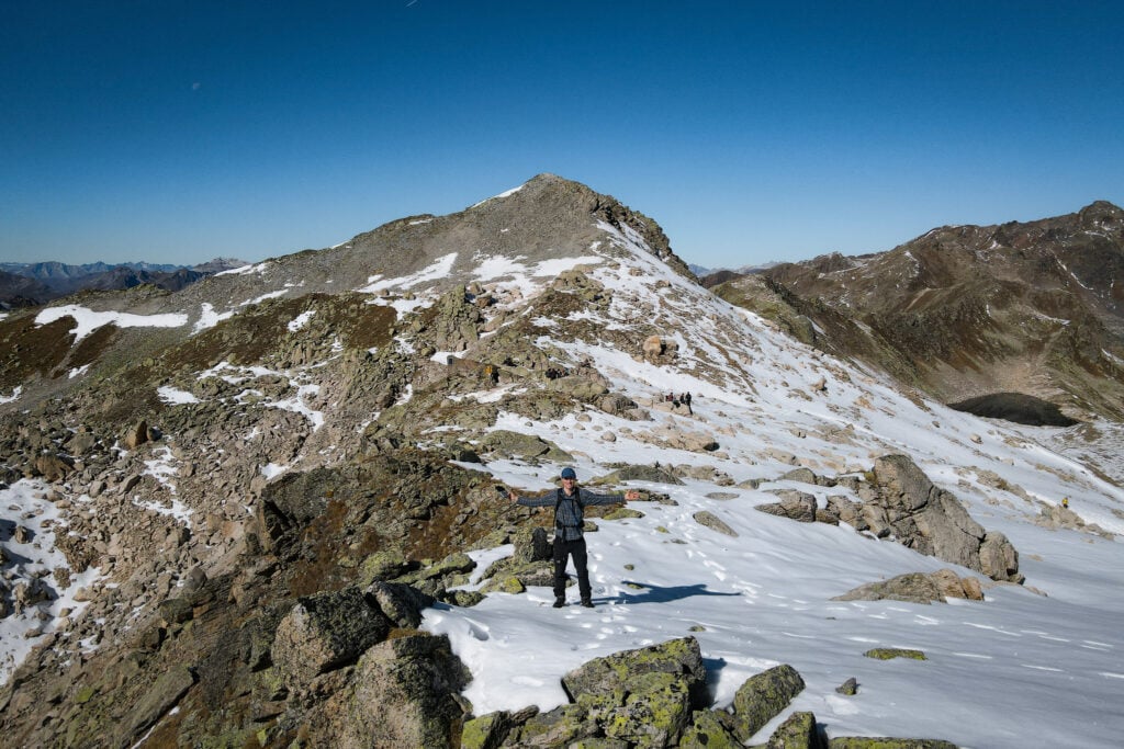 Dan stands on a snowy high mountain pass during one of the best hikes in Davos