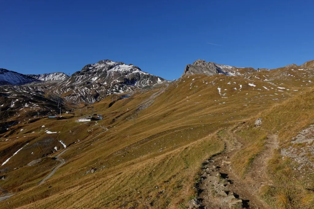 The Davos Panoramaweg winds through grassy hilly terrain towards snowy mountains