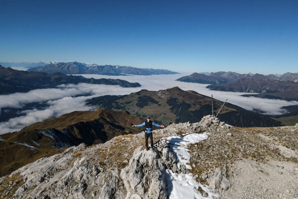Dan stands atop a mountain plateau with a cloud inversion in the background during one of the best hikes in Davos
