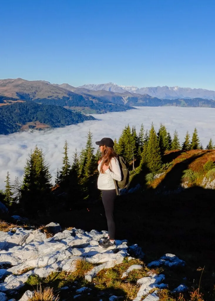 Beck stands on a rock platform looking towards mountains with a cloud inversion filling the valley in the background