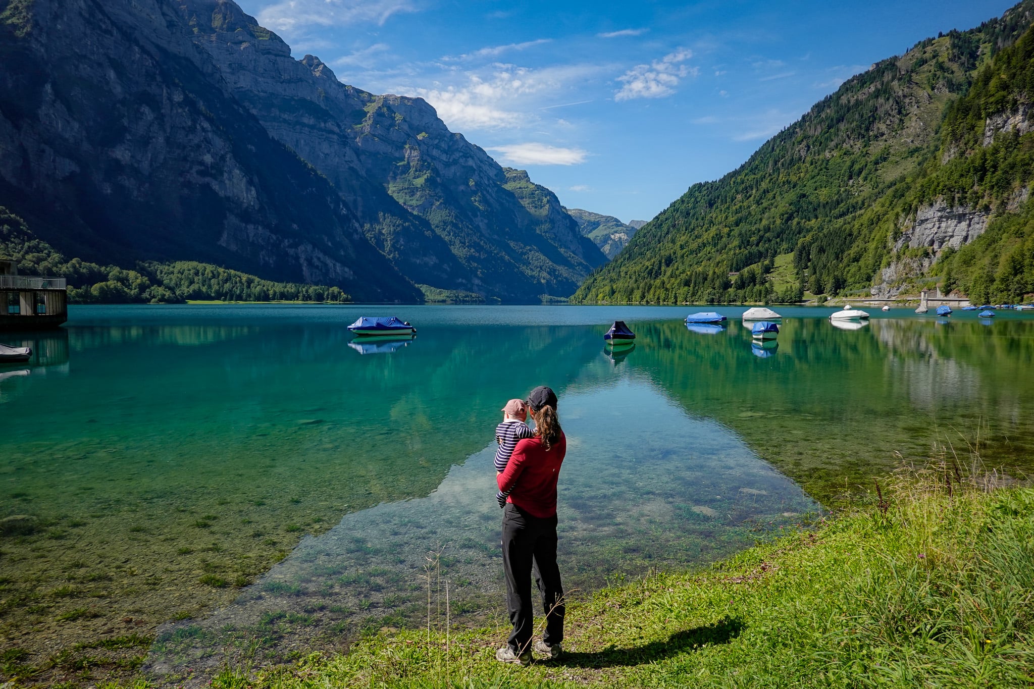 Beck holds a baby, overlooking a lake after doing a walk called Klöntalersee Rundwanderweg