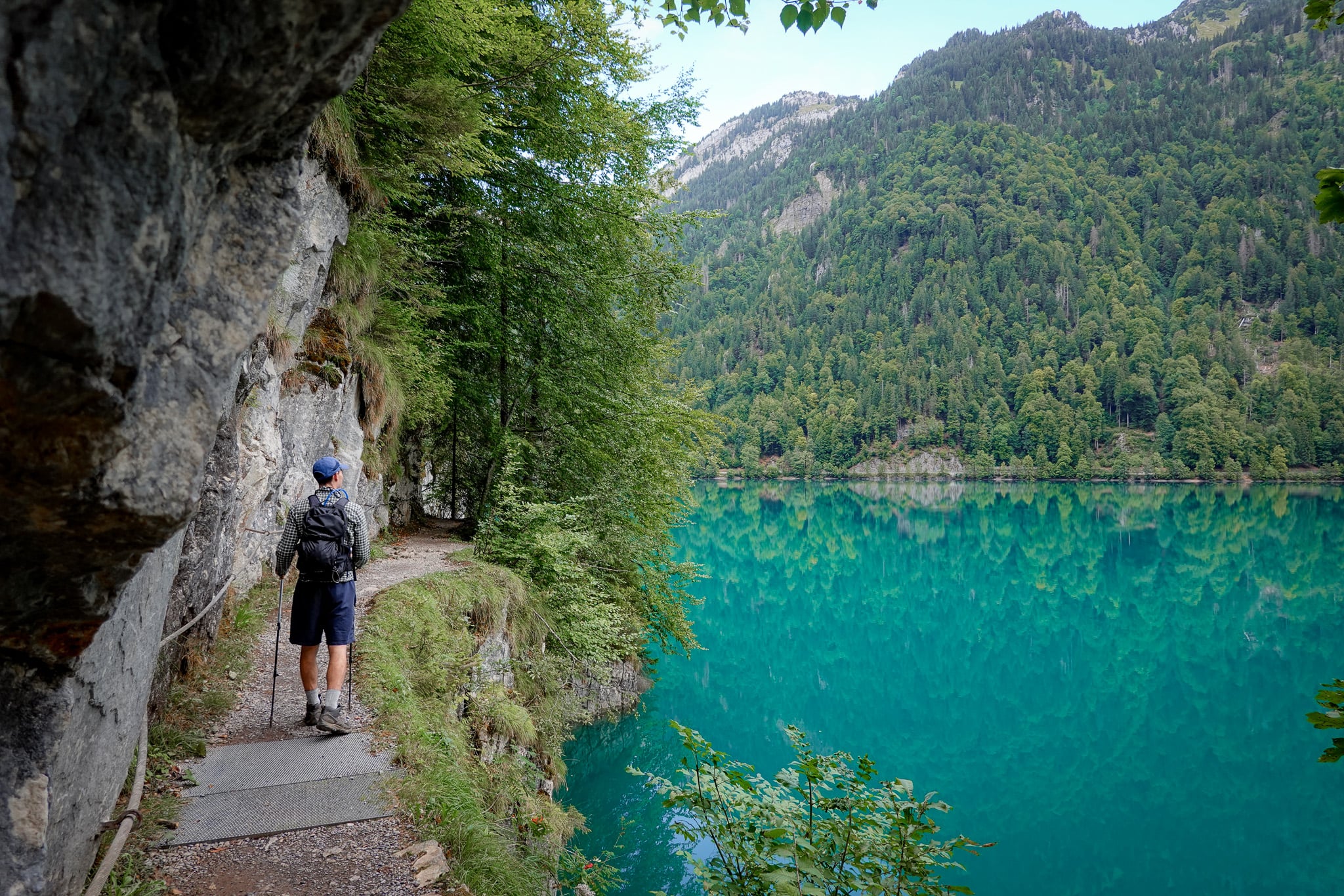 Dan walks between rockface and a lake during the Klöntalersee Rundwanderweg