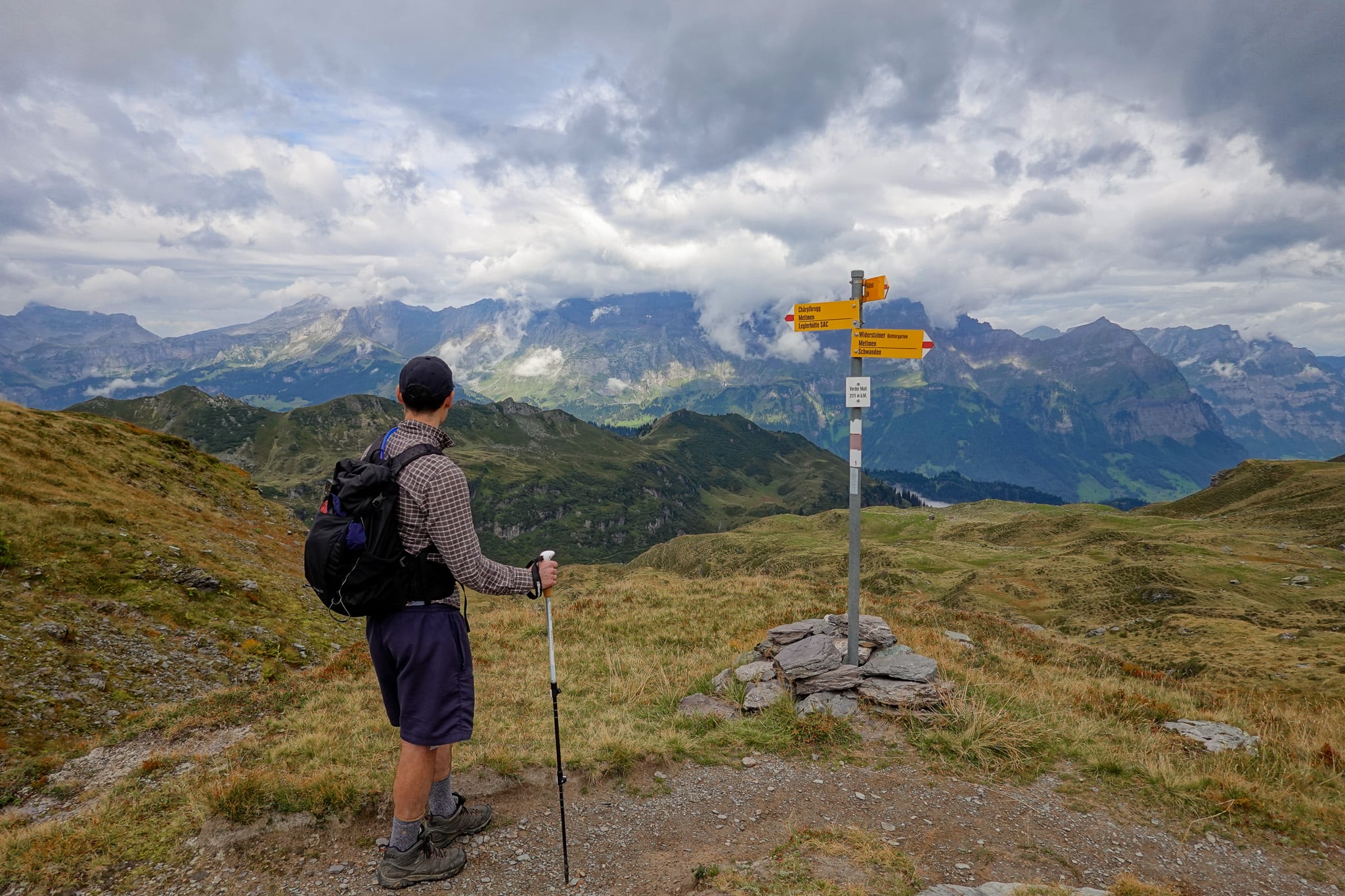 Dan stands near a signpost, looking towards mountains on the Kärpfwanderung